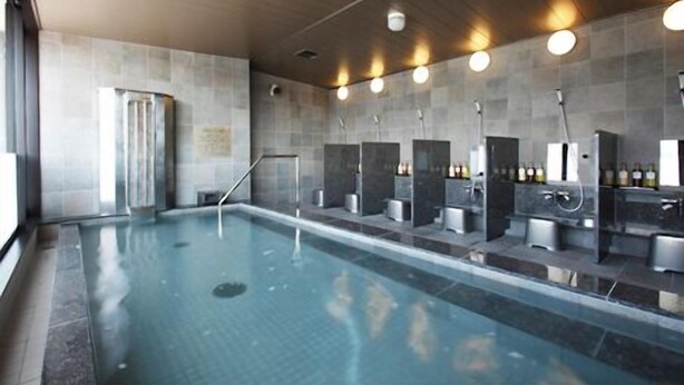 An indoor swimming pool with a modern design, including a long poolside area and multiple changing stations with mirrors and sinks. - Just ONE (Susono)