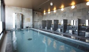 An indoor swimming pool with a modern design, including a long poolside area and multiple changing stations with mirrors and sinks.