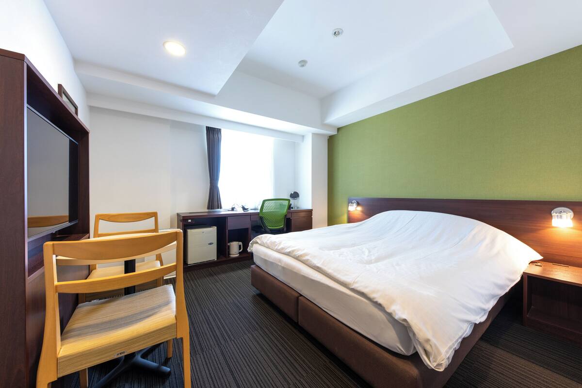 A hotel room with a bed, desk, chair, and a television.