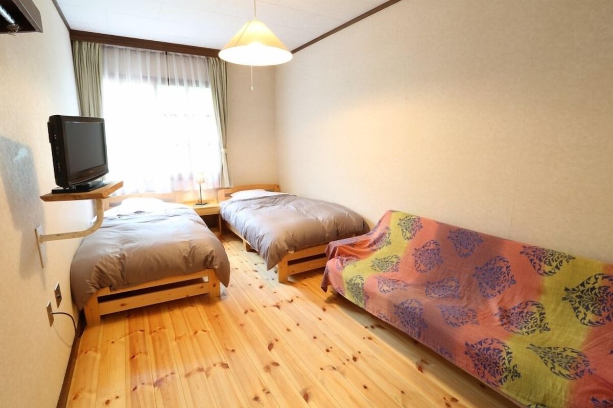 Una habitación pequeña con dos camas, un televisor sobre un mueble y una ventana con cortinas.