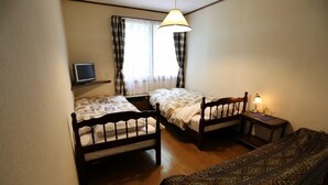 Ein Zimmer mit zwei Holzbett, einem Fernseher auf einem Regal, einer Lampe auf einem Nachttisch und einem gemusterten Teppich.