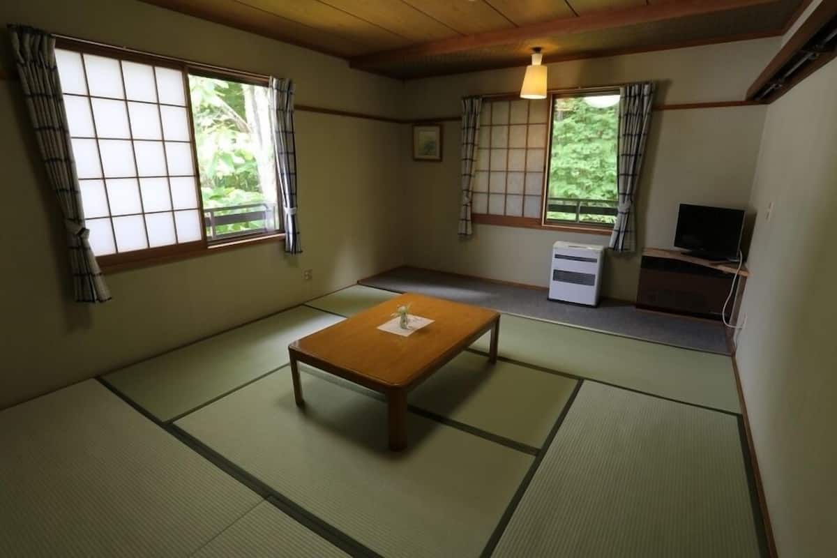 Una habitación tradicional japonesa con suelo de tatami, una mesa de madera baja, un televisor y puertas correderas con cortinas.