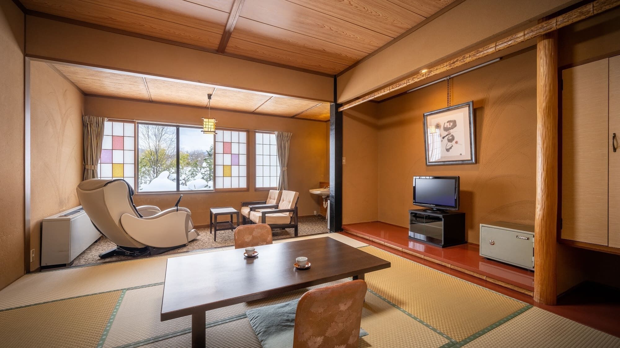 A traditional Japanese-style room with tatami flooring, a low table, chairs, a television, and a cabinet.