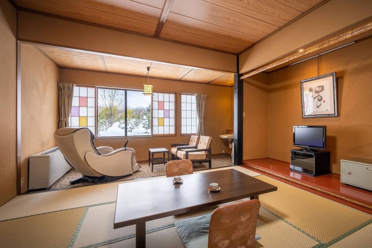 Una habitación tradicional japonesa con suelo de tatami, una mesa baja, sillas, un televisor y un armario.
