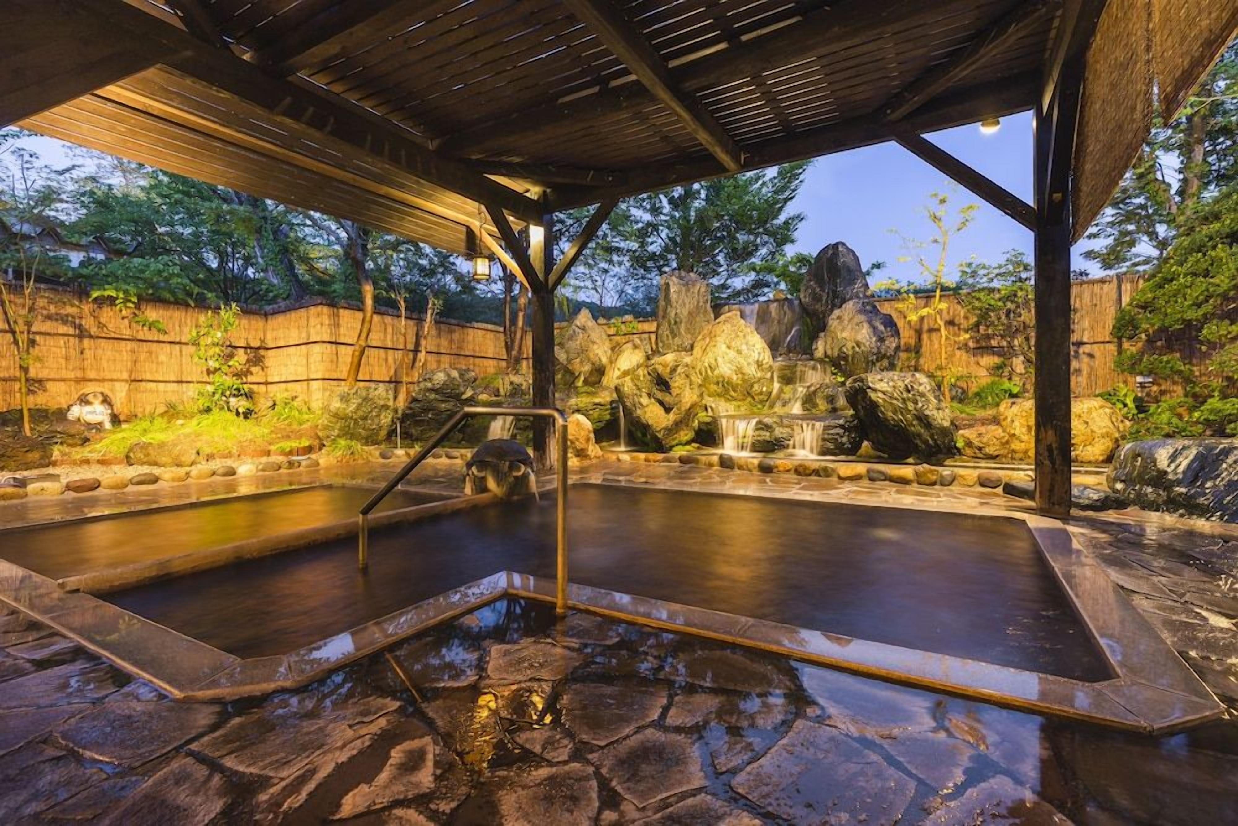 Un'area con sorgenti termali, una pergola in legno, pavimento in pietra e grandi rocce.