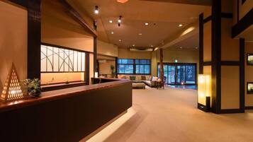 A reception area with a wooden reception desk, a large window with a view, and a seating area with a sofa and chairs.