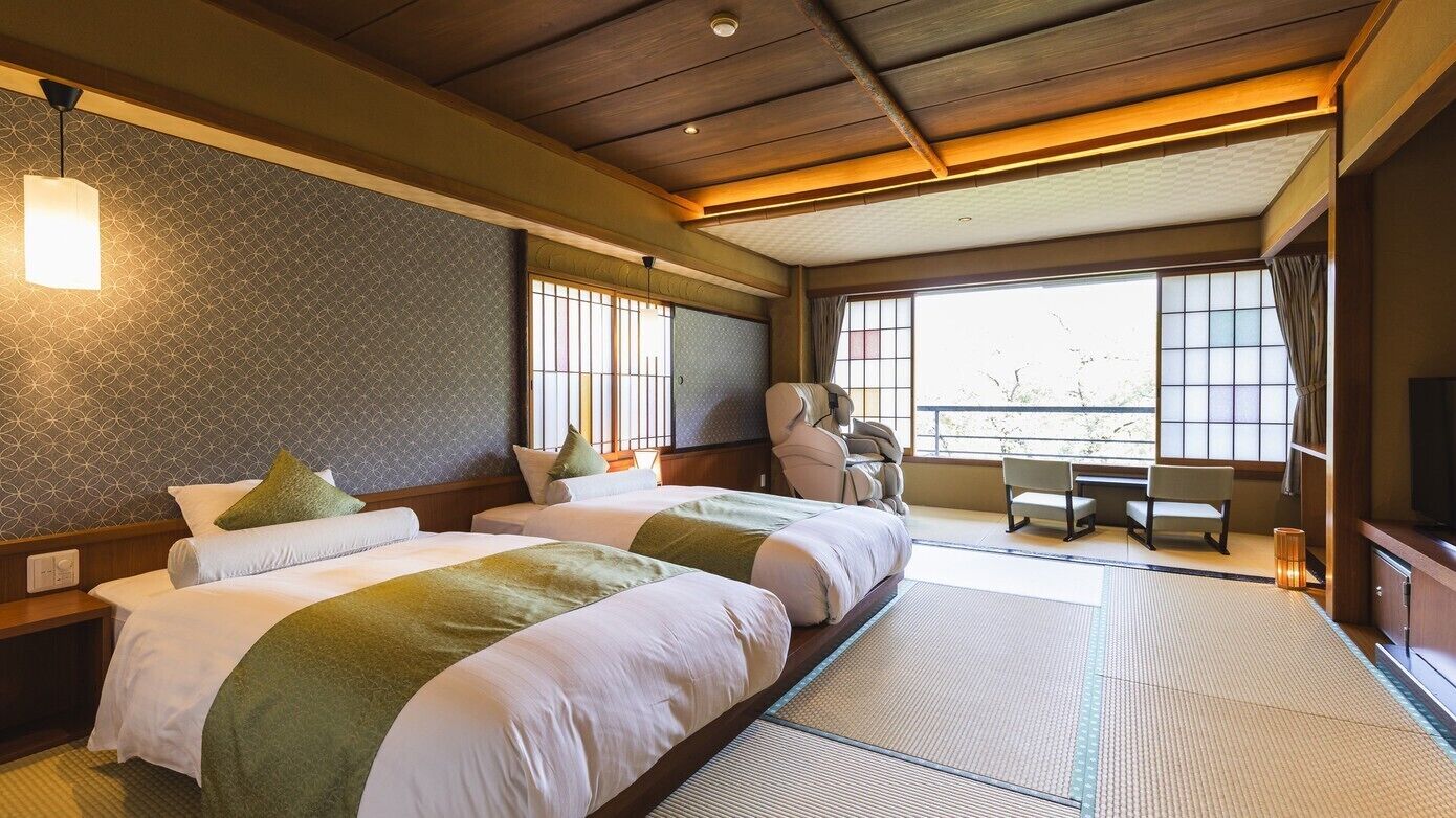 A hotel room with two beds, a desk, chairs, a television, and large windows.