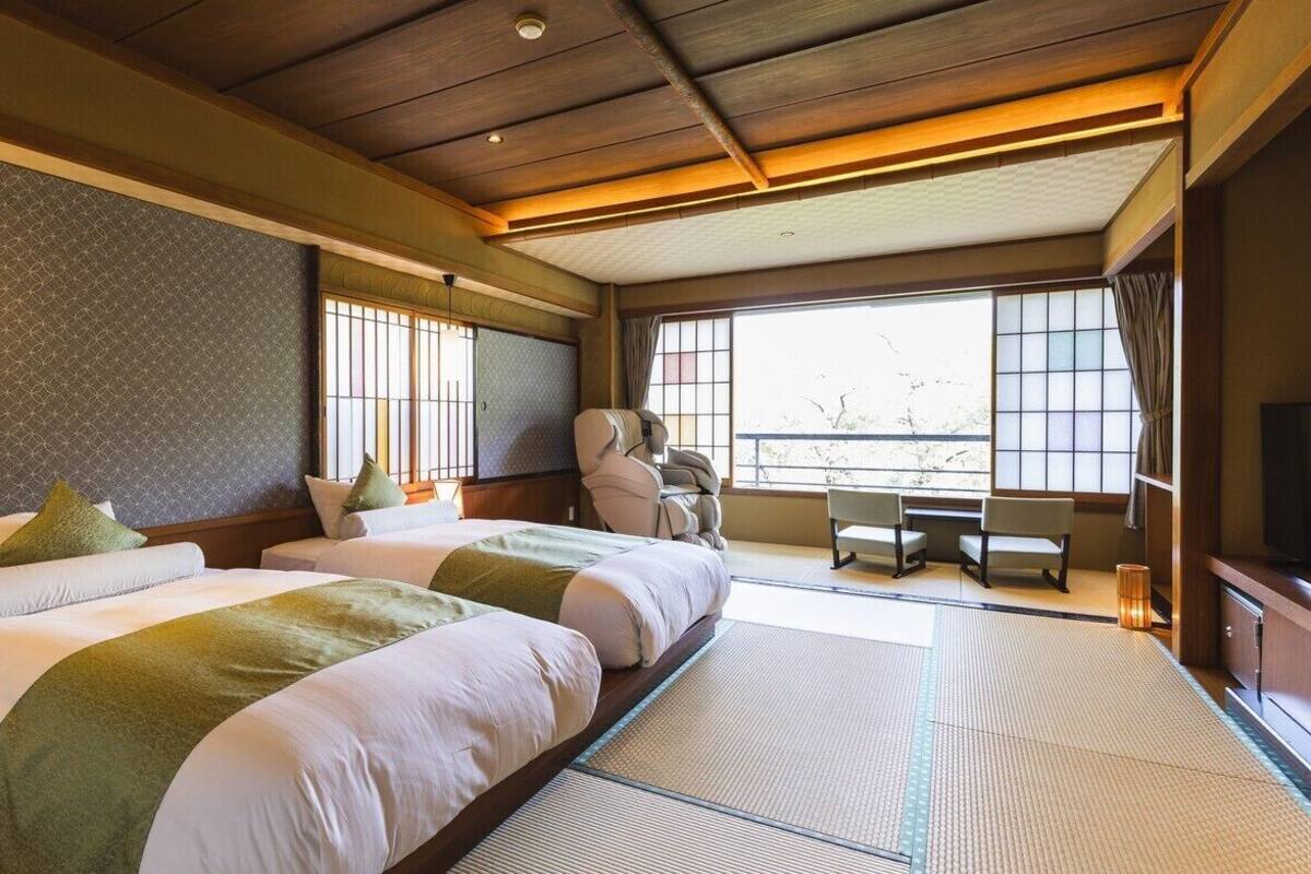 Habitación de hotel con dos camas, un escritorio, sillas, un televisor y ventanas amplias.