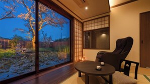 A room with tatami flooring, a low table with a cushion, a chair, a sliding glass door with a view of cherry blossoms, and a traditional Japanese sliding door. - Kajikaso (Yonezawa)