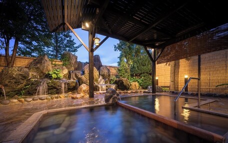 A hot spring area with a wooden deck, a stone pool, and a waterfall.