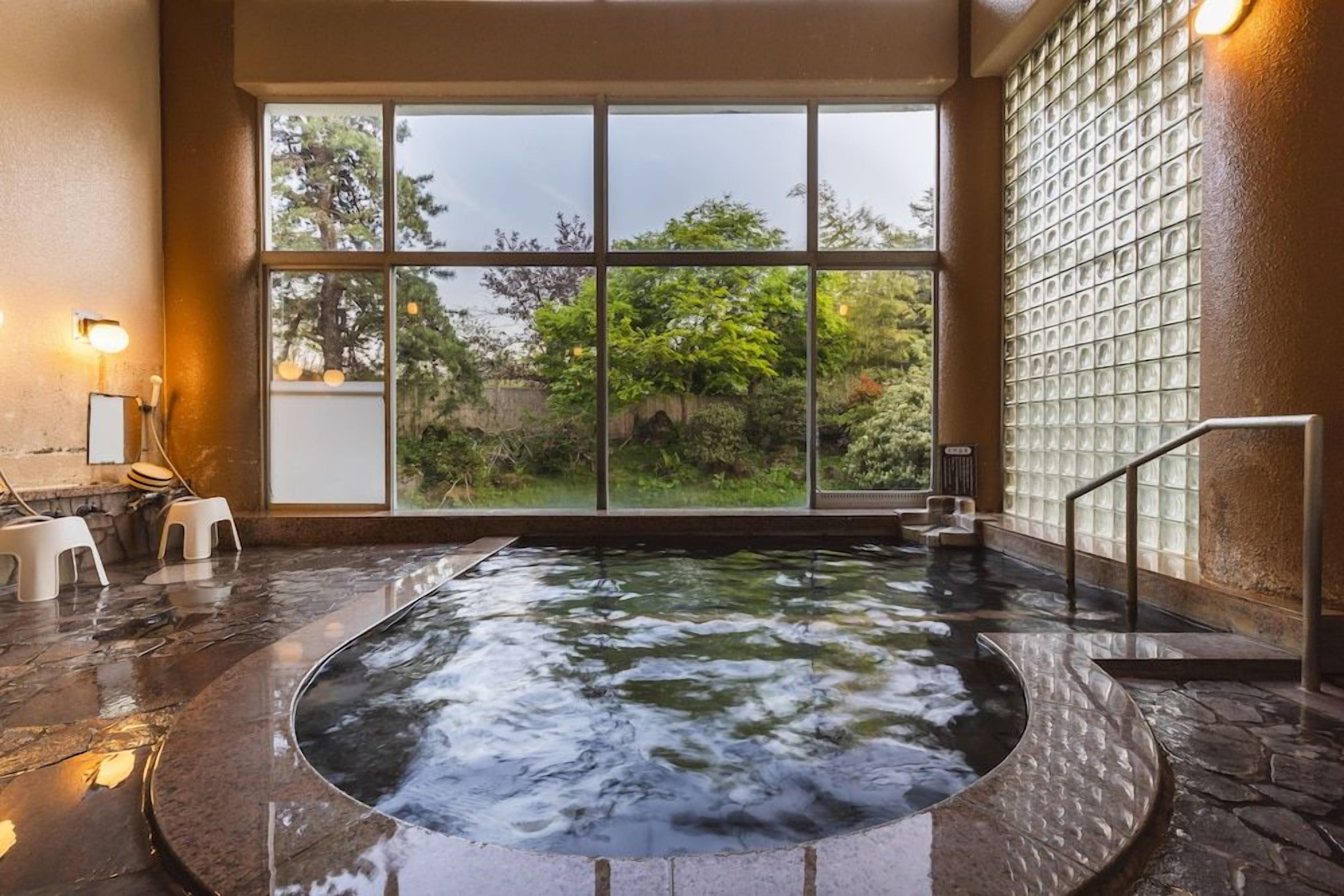 A hot tub with a view of the outdoors, surrounded by stone flooring and a glass wall.