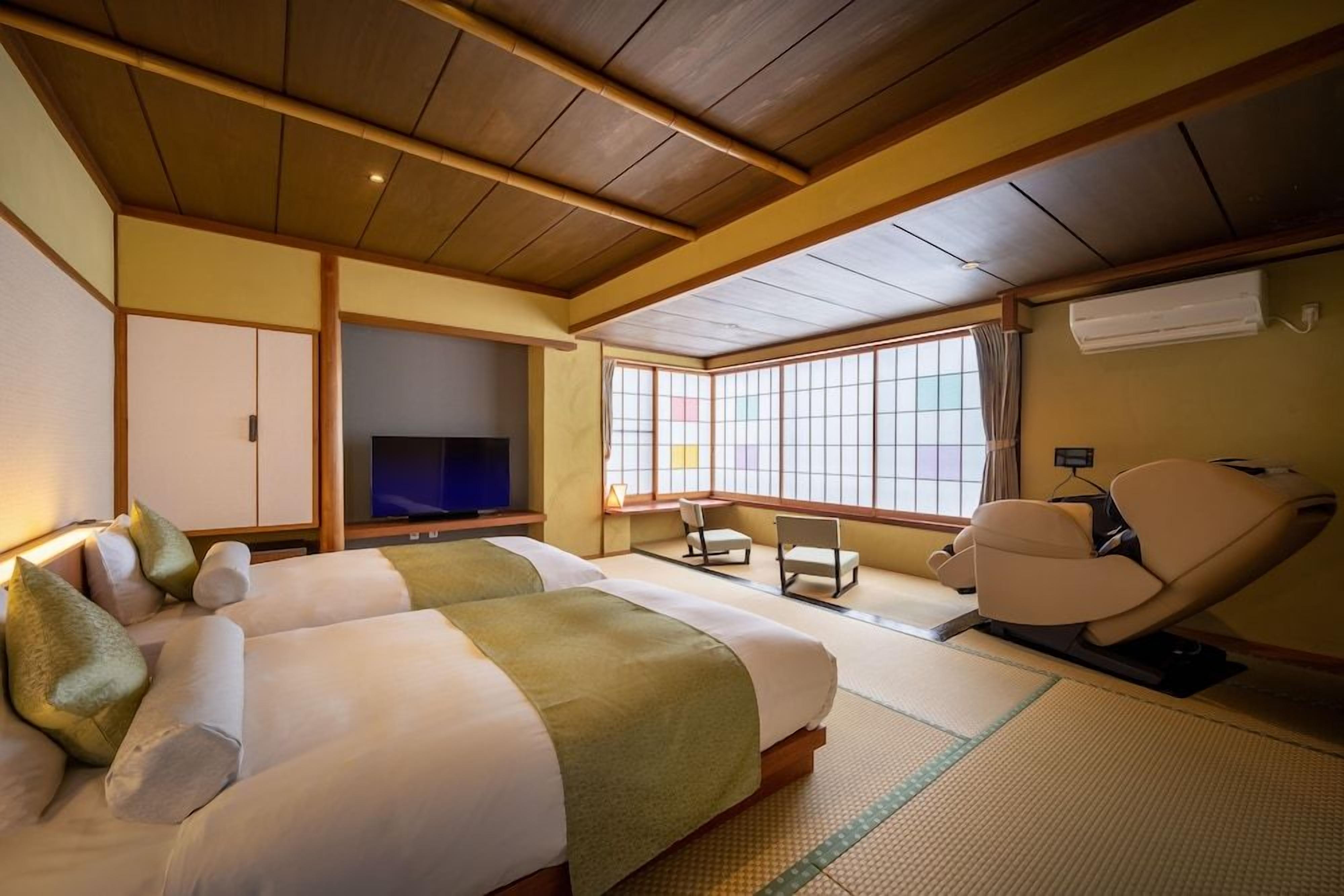 Een traditionele Japanse kamer met tatami vloerbedekking, een televisie, een massagestoel en een schuifdeur.