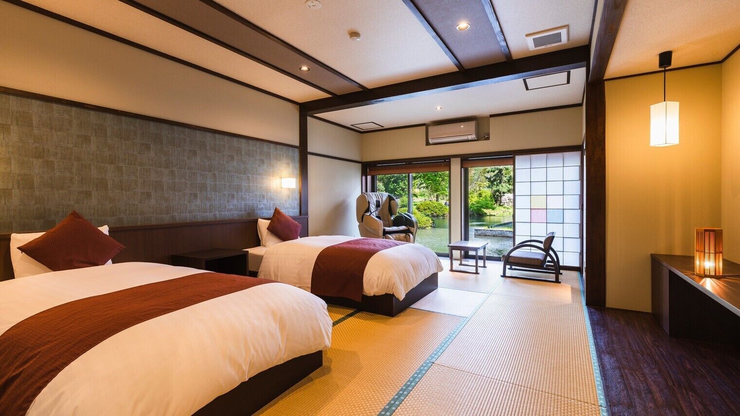 A hotel room with two beds, a small table, a chair, and a view of the outdoors.