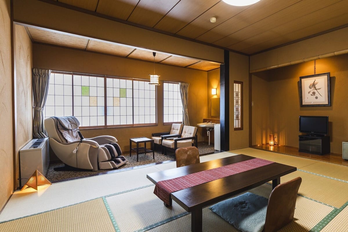 Una habitación de estilo japonés tradicional con suelo de tatami, sillón de masajes, una pequeña mesa, televisor y caja fuerte.