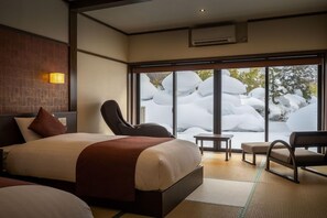 A hotel room with a bed, seating area, and a view of snow-covered rocks. - Kajikaso (Yonezawa)