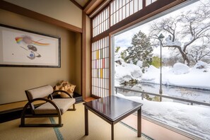 A traditional Japanese room with tatami flooring, a low table, a chair, and a view of a snowy landscape through a shoji screen. - Kajikaso (Yonezawa)