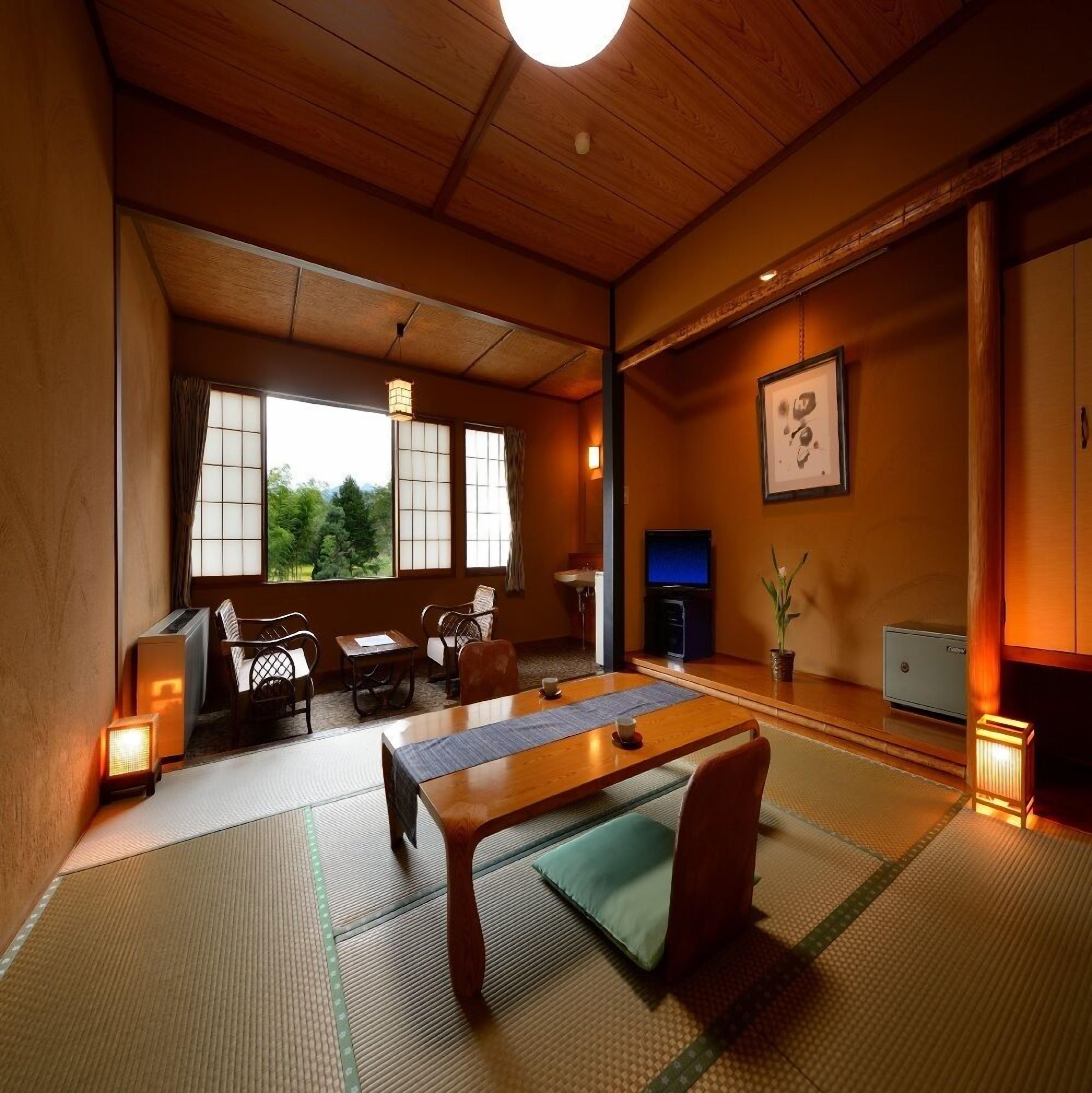 Perinteinen japanilainen huone, jossa on tatamimatto, matala pöytä, tuoleja, televisio ja näkymä vehreään maisemaan.