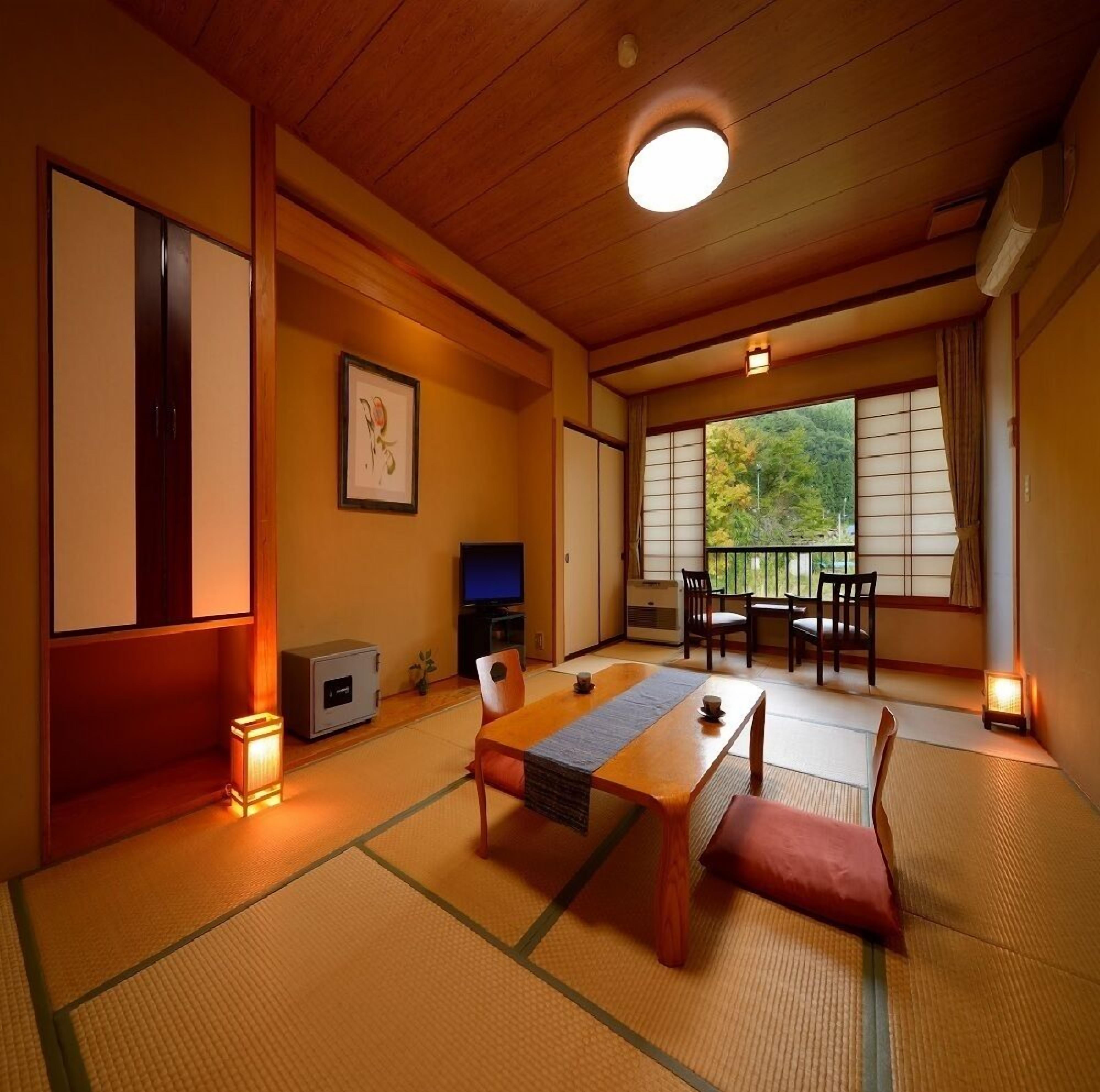 Perinteinen japanilainen huone, jossa on tatamimatto, matala pöytä, tuoleja, televisio ja ikkuna, josta avautuu näkymä puita kohti.