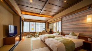A traditional Japanese-style hotel room with tatami flooring, a television, two beds, and a view of the city. - Kajikaso (Yonezawa)