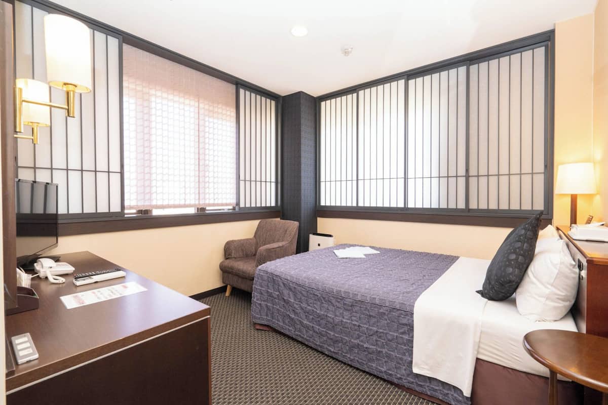 A hotel room with a bed, a desk, a chair, and a TV.