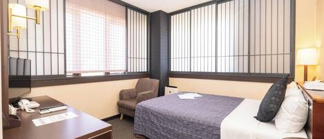 Quarto de hotel com cama, escrivaninha, cadeira e televisão.