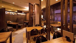 A modern restaurant with wooden tables and chairs, a bar area with bottles, and a cozy ambiance.