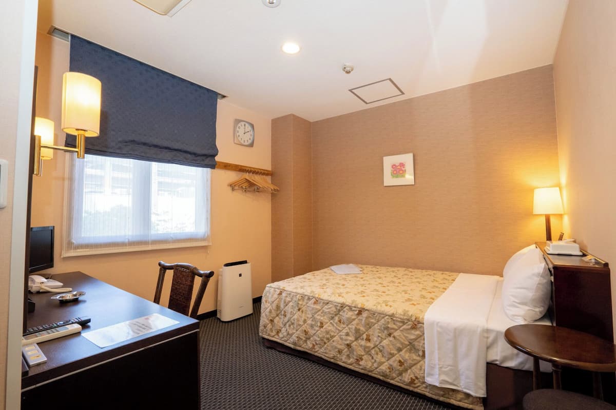 A hotel room with a bed, desk, chair, and a small table.