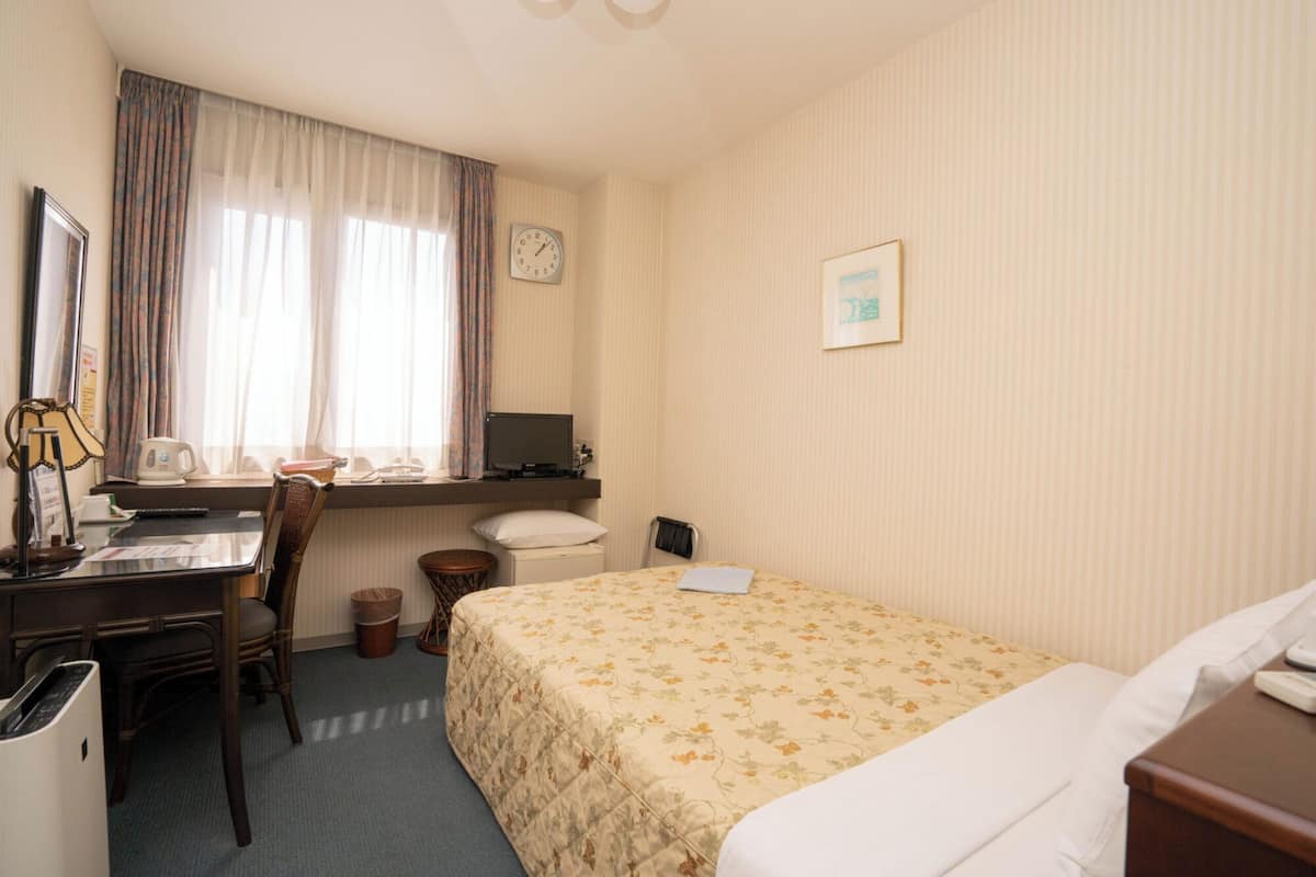 A hotel room with a bed, a desk, a chair, a clock, and a window with curtains.