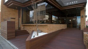 A modern building with a brick facade, wooden steps leading to a glass entrance, and a small tree in a planter.