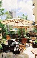 Un área de patio al aire libre con mesas y sillas, rodeada de vegetación y un edificio al fondo.