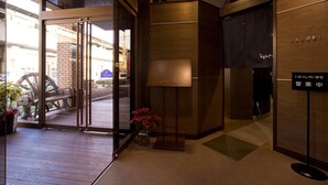 A hotel entrance with a wooden reception desk, a glass door entrance, and a sign indicating a business center.