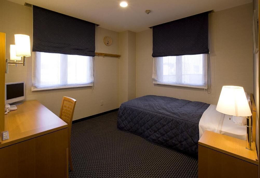 A hotel room with two beds, a desk, a chair, a TV, and a lamp.