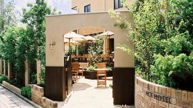 A hotel entrance with outdoor seating, a brick wall, and greenery.