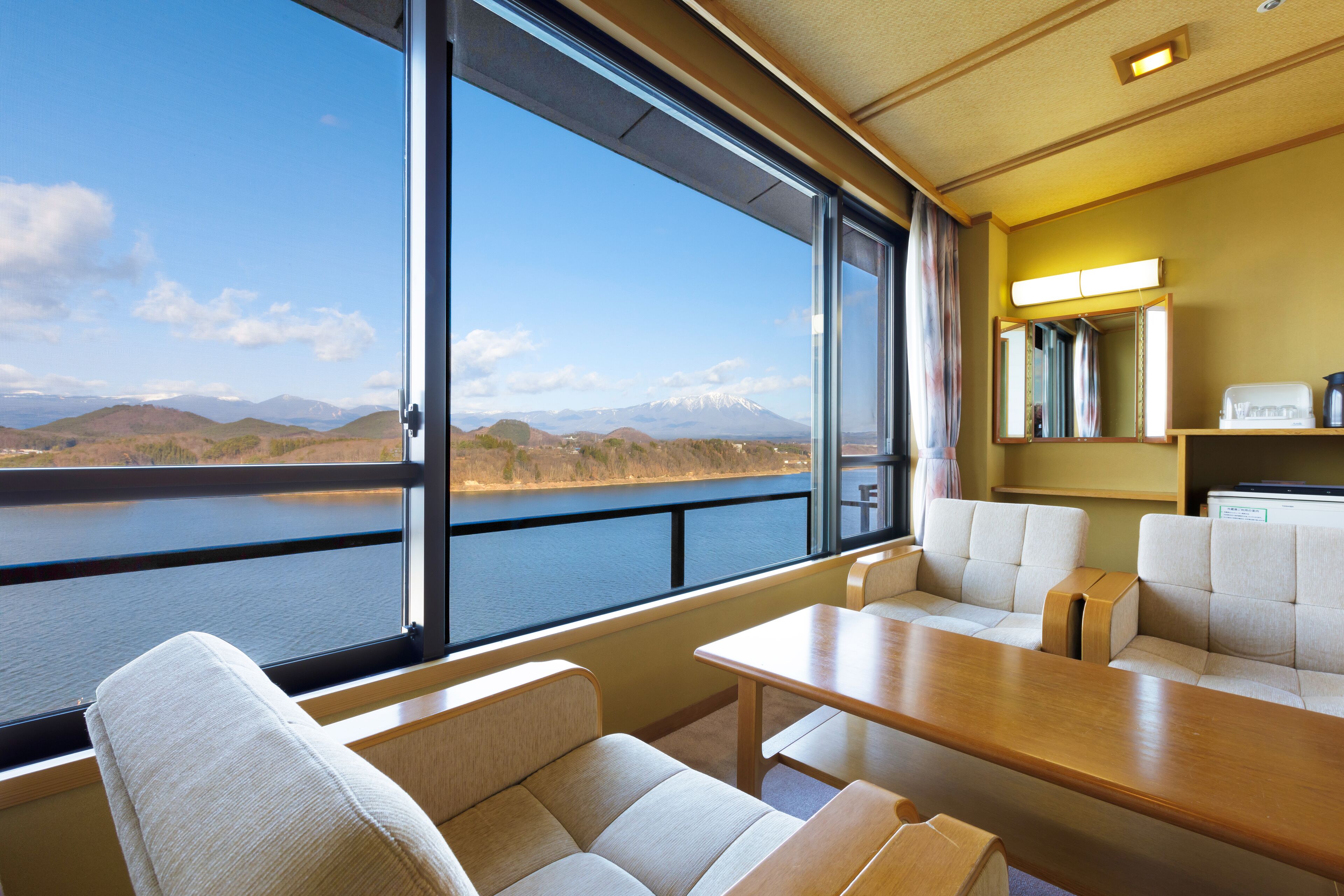 Habitación con un ventanal grande que ofrece vistas a un lago y montañas. Hay dos sofás y una mesa.