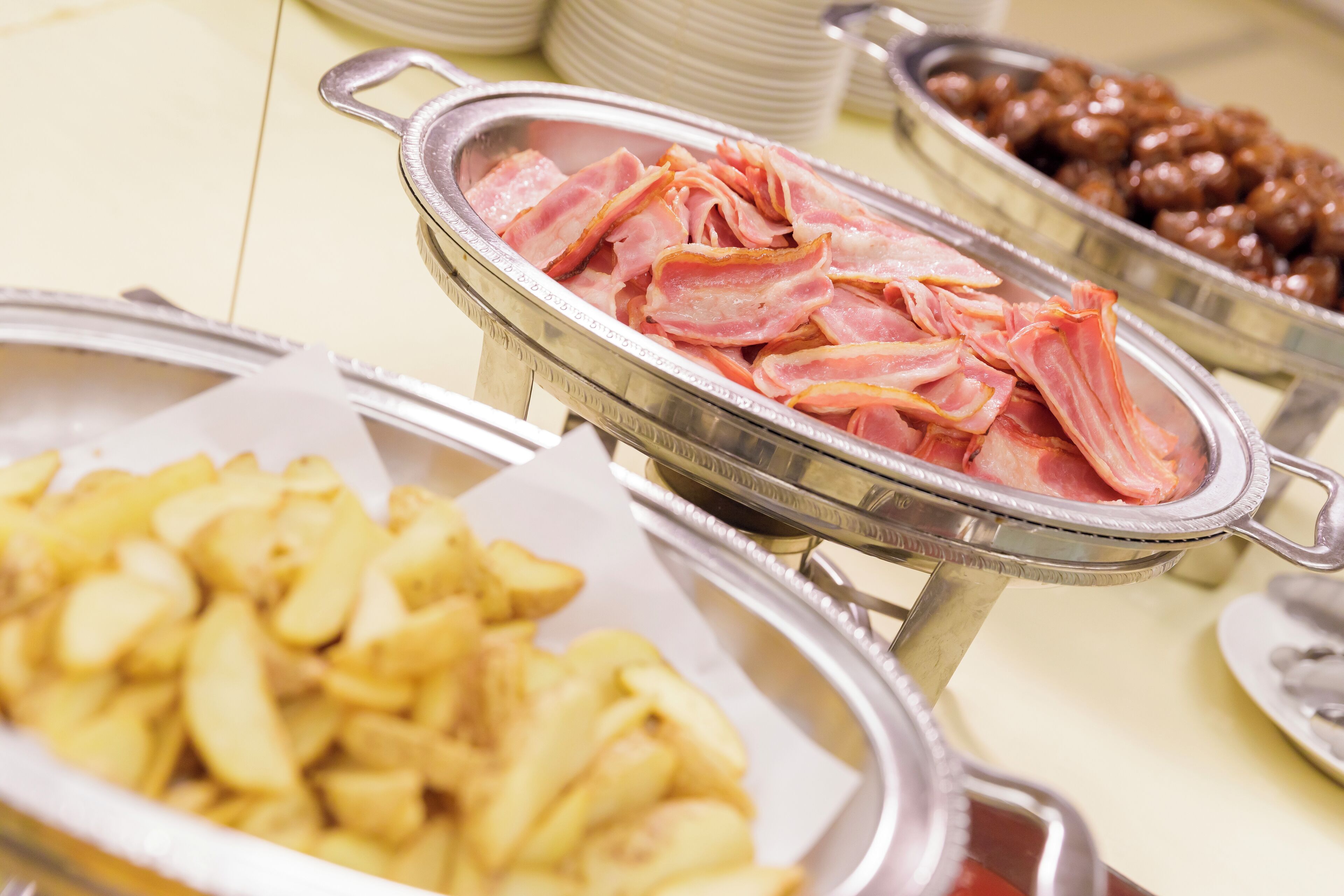 A buffet with various food items including bacon, potatoes, and a dish that appears to be a type of bean salad.