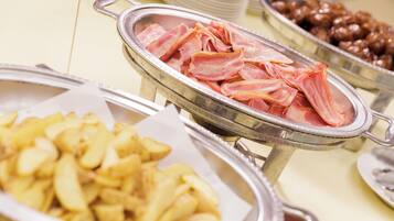 Un bufé con diversos alimentos, incluyendo tocino, papas y un plato que parece ser una ensalada de legumbres.