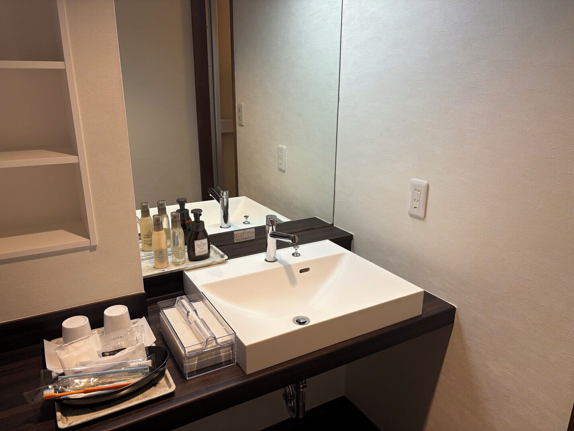A bathroom with a white sink, a mirror, and toiletries on the counter.