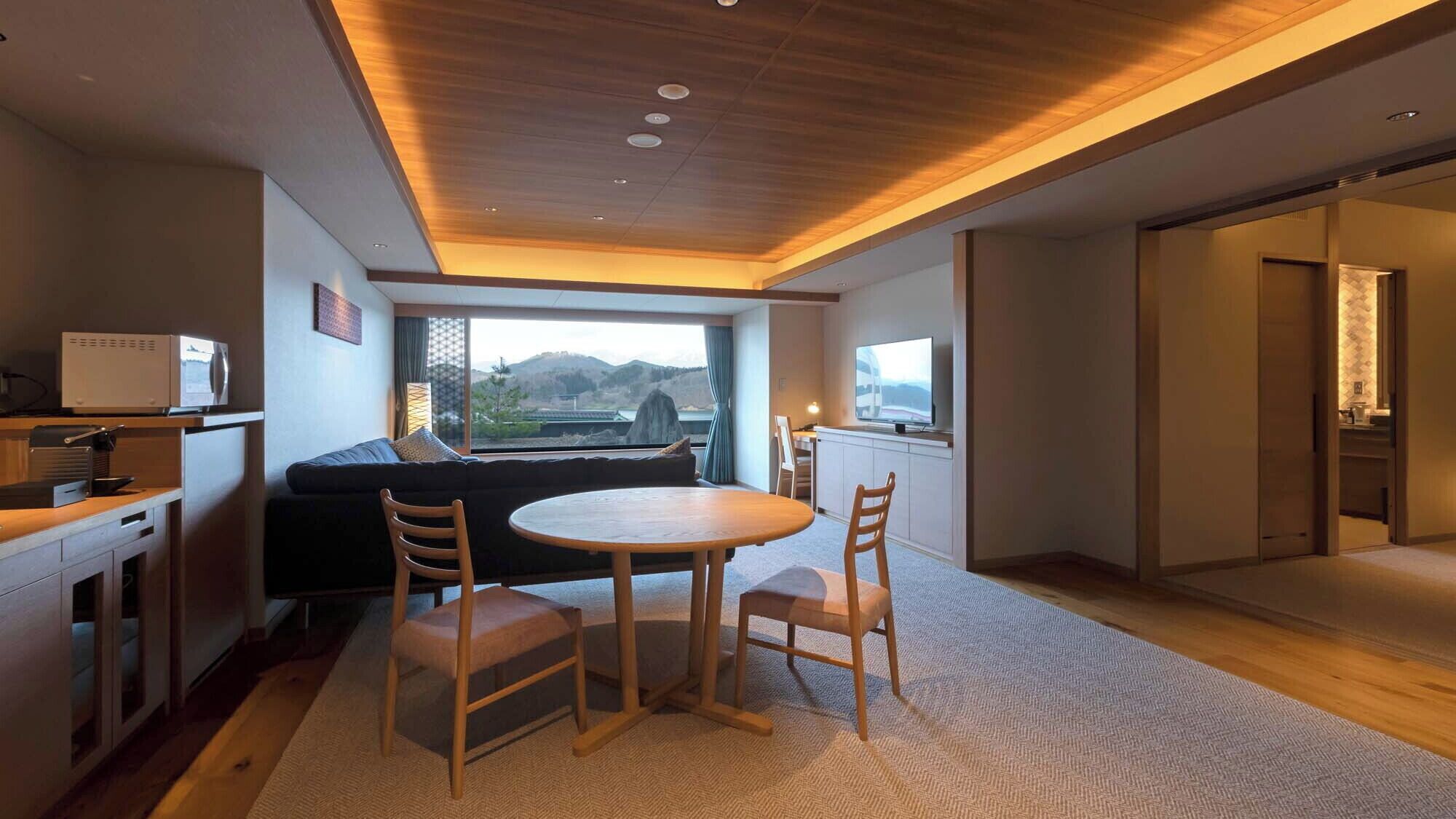 Une chambre d’hôtel moderne dotée d’un coin repas, d’un canapé, d’une télévision et offrant une vue sur les montagnes.