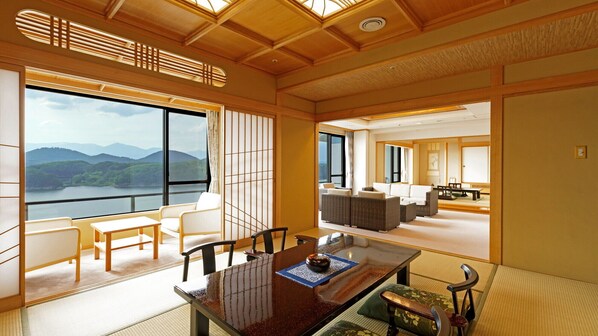 Una habitación tradicional japonesa con suelo de tatami, una mesa baja con un juego de té y vistas a un lago y montañas.
