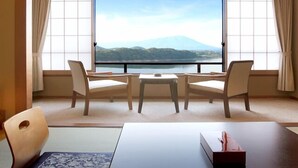 A hotel room with a large window offering a view of a mountain and lake. There are two chairs and a small table in the room. - Hotel Shion (Morioka)