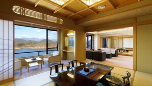 A traditional Japanese-style room with tatami flooring, a low table with a tea set, and a view of a lake and mountains through large windows. - Hotel Shion (Morioka)