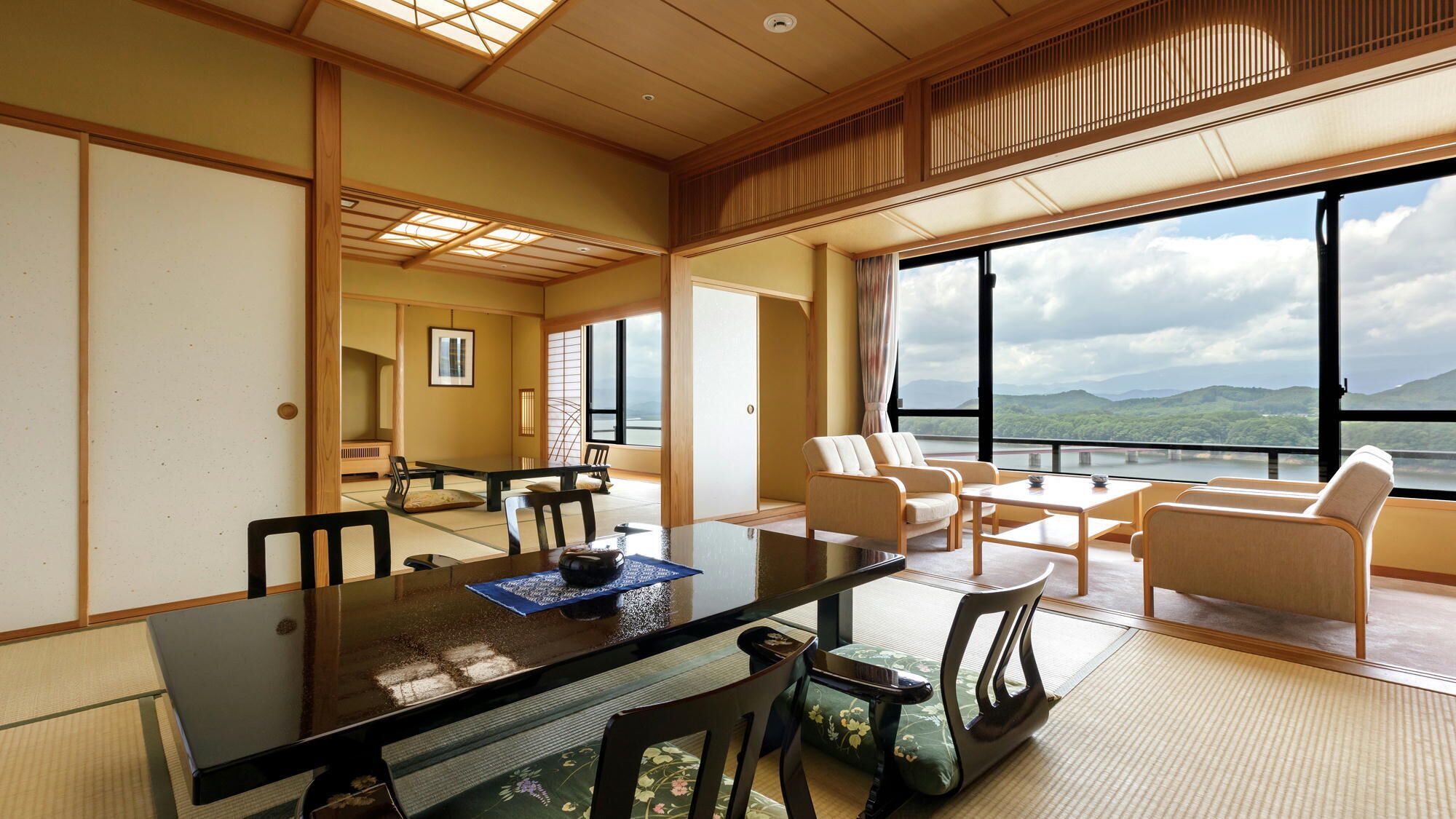 A traditional Japanese-style room with tatami flooring, a low table, and a view of a river and mountains.