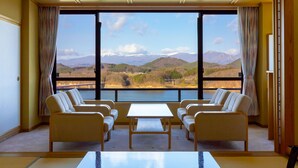 A room with a large window offering a view of mountains and a lake. There are two sofas and a table in the room. - Hotel Shion (Morioka)