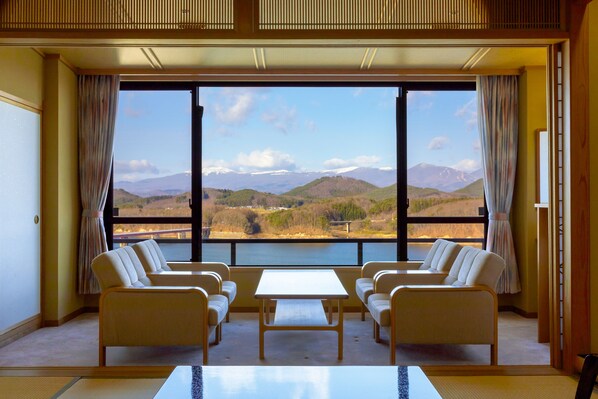 Habitación con un ventanal grande que ofrece vistas a montañas y un lago. Hay dos sofás y una mesa en la habitación.
