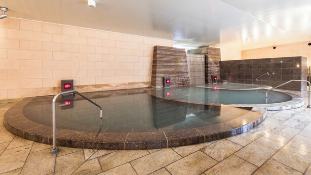 A spa area with two hot tubs, a control panel, and a tiled wall. - Hotel Ichii (Kusatsu)