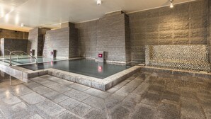 A modern indoor pool area with stone walls and a glass railing. - Hotel Ichii (Kusatsu)