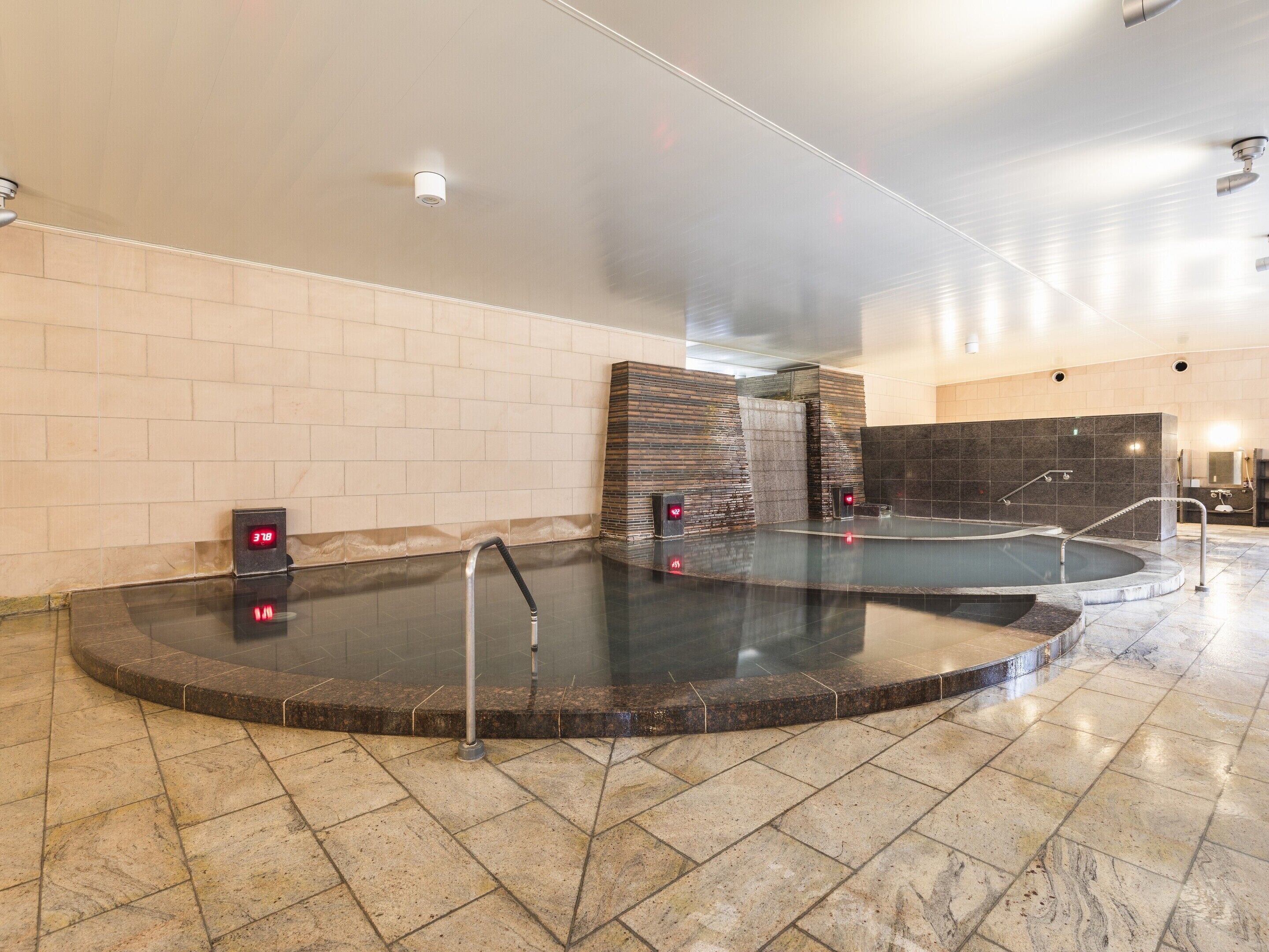 Zona de spa con dos jacuzzis, una pared con diseño texturizado y un reloj digital que muestra la hora.