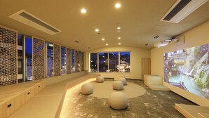A modern interior with a curved seating area, large windows, and a projection screen displaying a scenic view. - Hotel Ichii (Kusatsu)