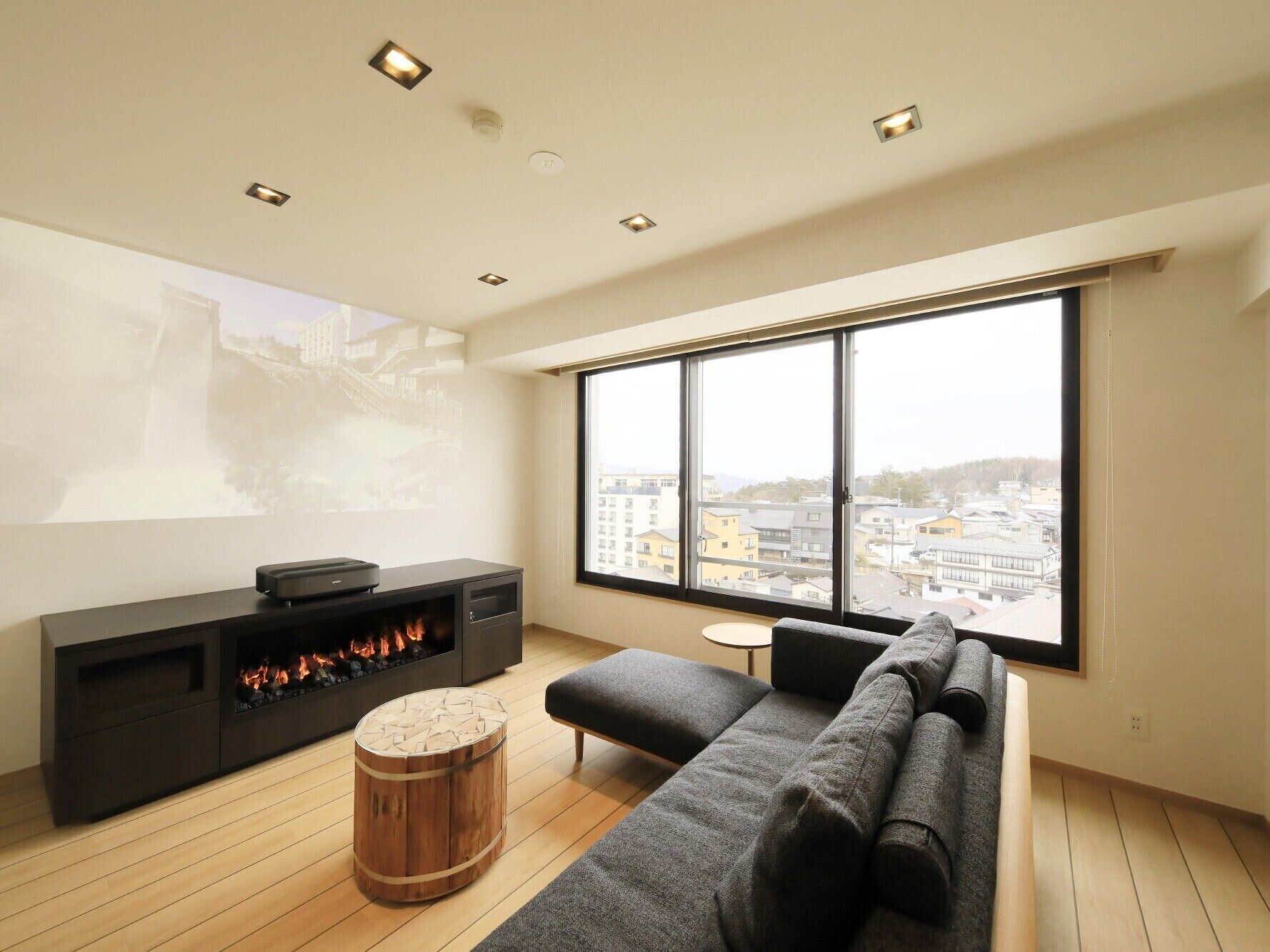 A modern living room with a large window, a fireplace, and a projector screen.
