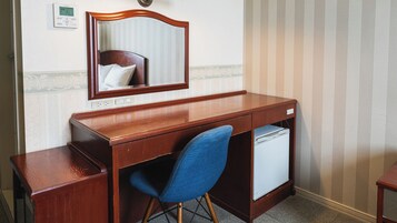 Un escritorio de madera con un espejo, una silla azul y un mini refrigerador blanco.
